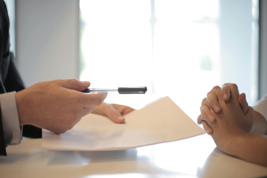 An image showing an intellectual property lawyer passing a client some papers to sign, regarding the protection of their intellectual property.
